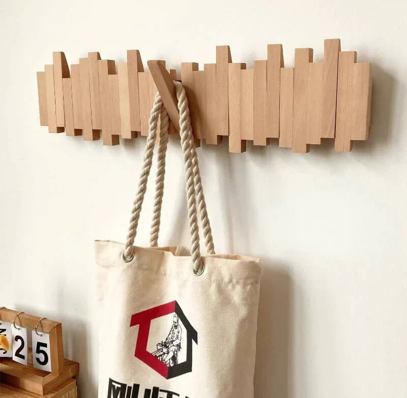 Natural wood wall coat rack with five hooks and a beige canvas bag with rope handles hanging from it