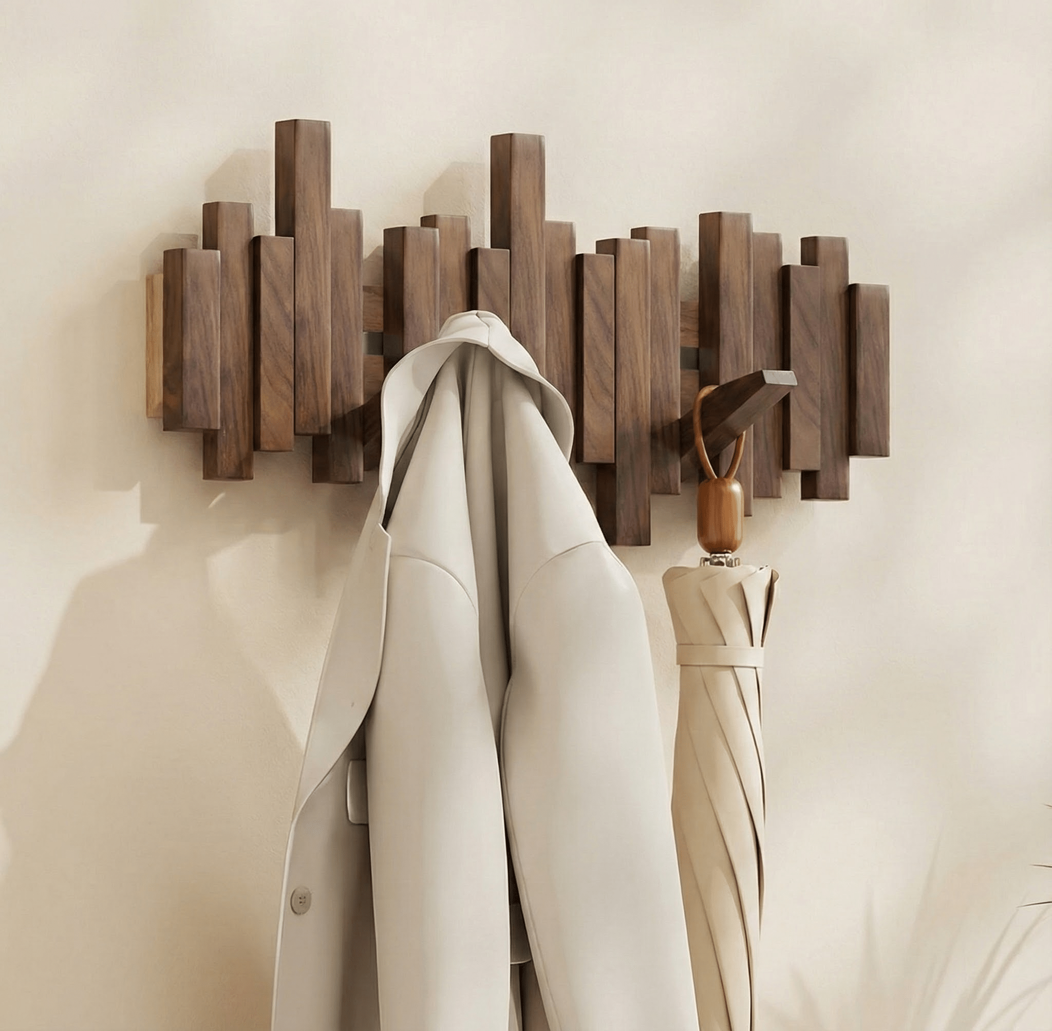 Natural finish solid wood wall coat rack with multiple stacked rectangular blocks and five hooks, a coat hangs on the left and an umbrella on the right