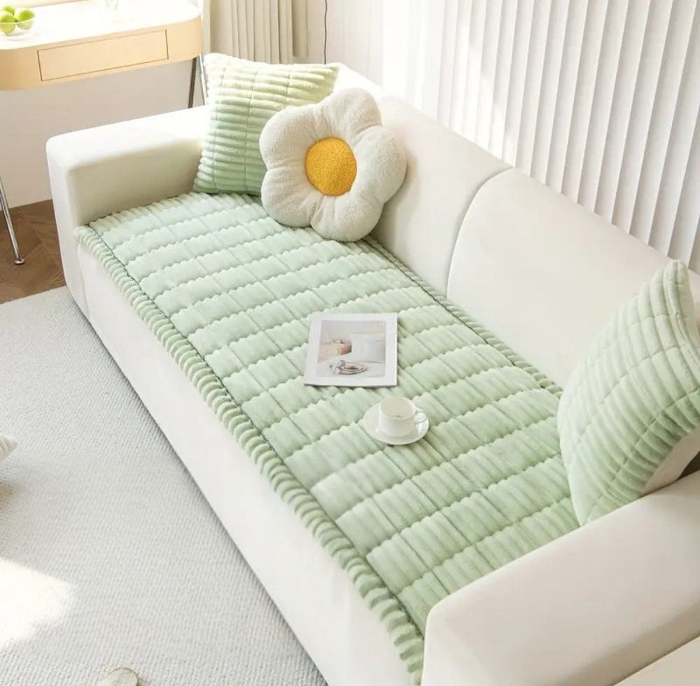 White sofa covered with a mint green quilted cover with hand pleated edges and matching cushions, a daisy shaped pillow and a small cup on the cover