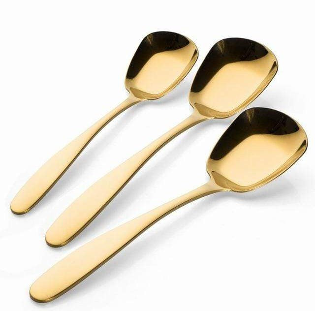 <Three gold colored stainless steel serving spoons with a polished finish on a white background>